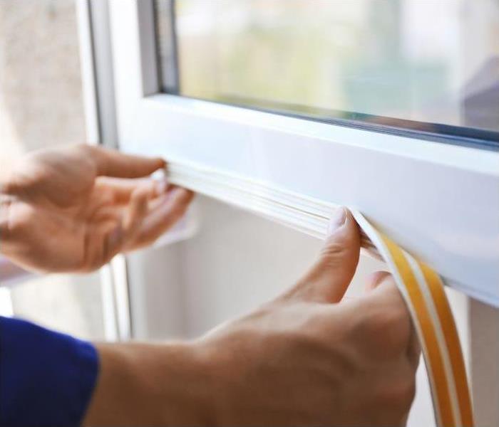 a person placing weather stripping on a white window